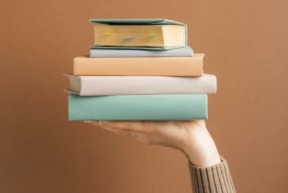 a hand holding many books in front of the wall